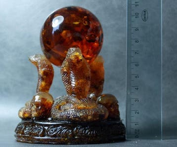 3 Baltische amber-kobras die een amberbal vasthouden. -