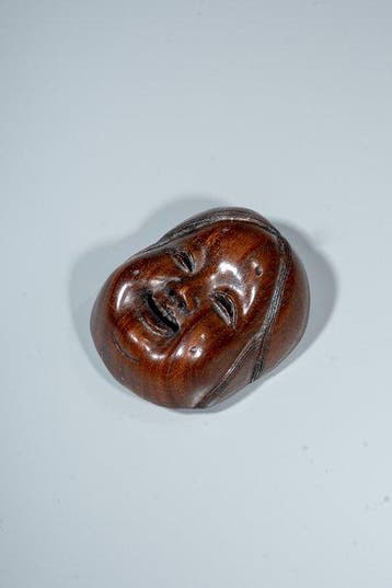 Een Japanse netsuke van buxushout die het masker van Okame