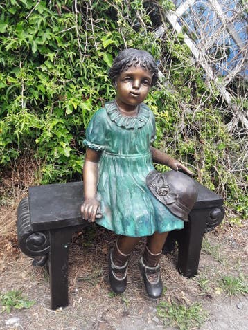 Bronzen meisje op bankje.